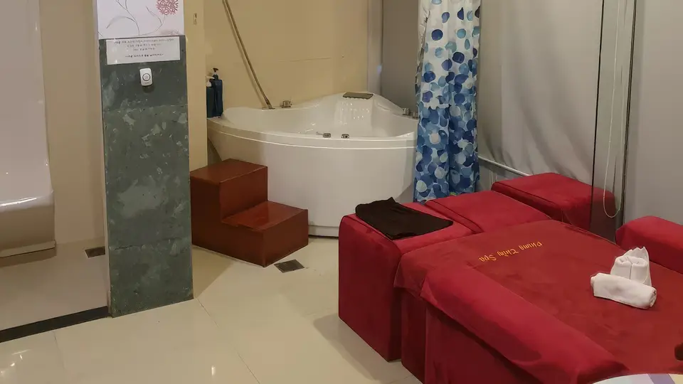 다낭 풍투이 스파 코너 자쿠지 욕조와 나란히 놓인 두 개의 붉은 마사지 베드, 대리석 기둥과 샤워 커튼이 어우러진 스파 룸