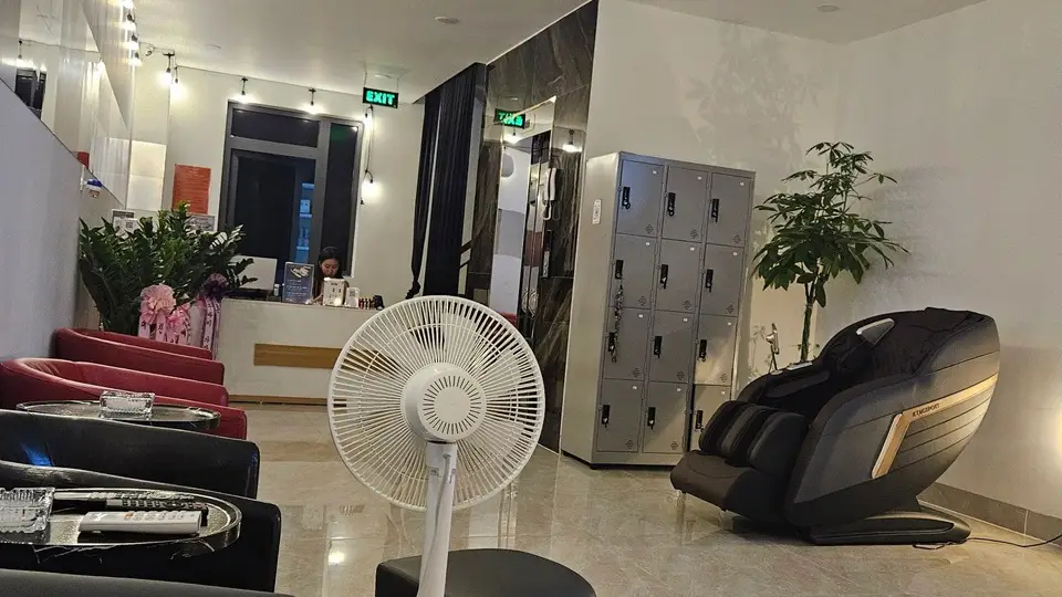 호치민 슈퍼맨 마사지 슈퍼맨 마사지 로비 전경 — 붉은 소파와 검정 안락의자, 무인 사물함, 고급 전자동 마사지 체어, 리셉션 직원이 배치된 밝고 넓은 대기 공간